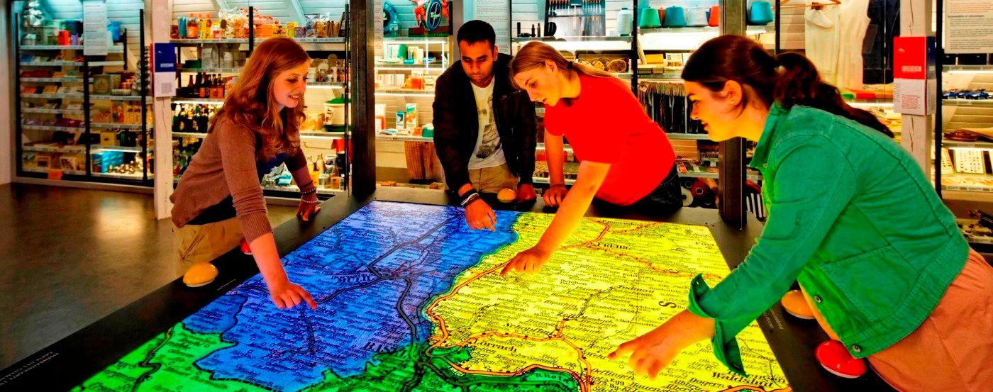 Quatre personnes explorent une carte illuminée sur une grande table au musée