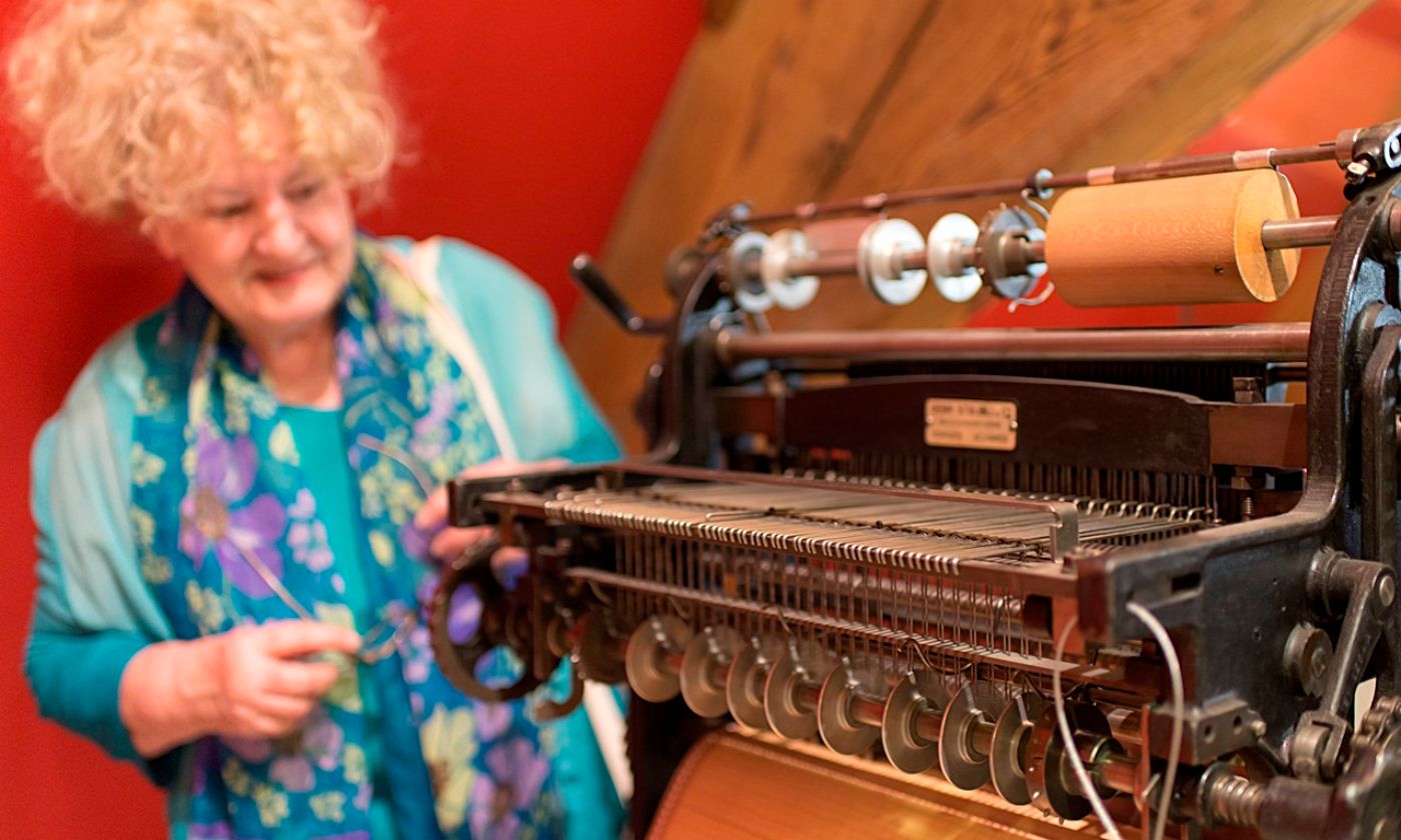 A woman examines an old weaving machine with red walls in the background