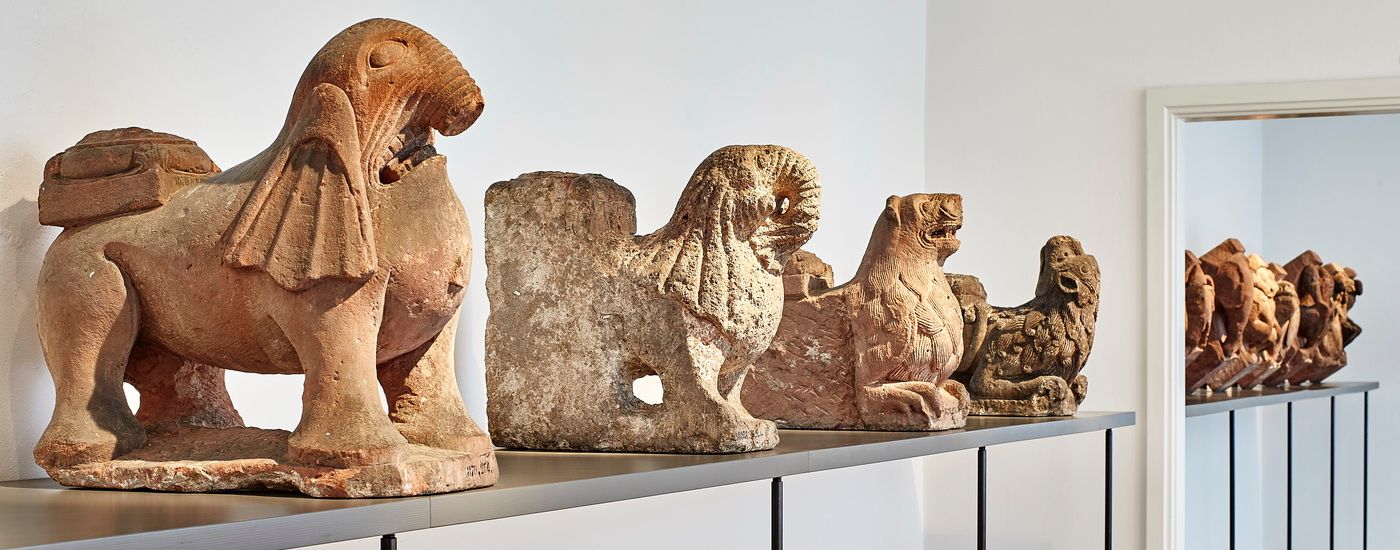 A row of medieval stone lion sculptures stands on a shelf in an exhibition room