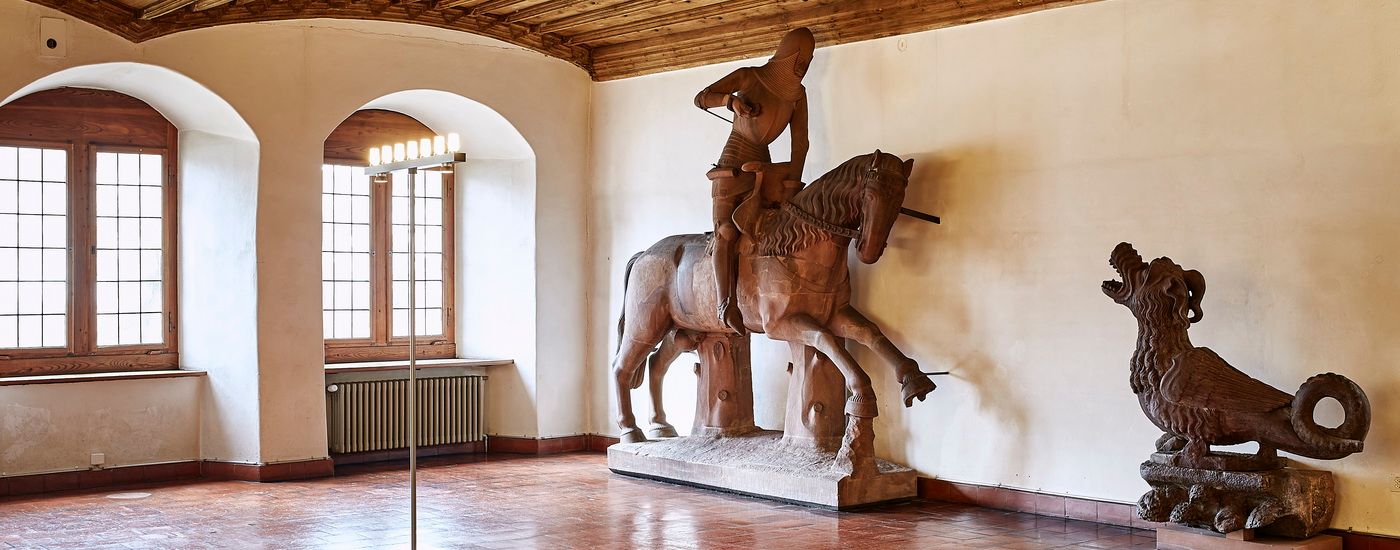 A stone knight rides a horse beside a mythical creature in a sunlit room