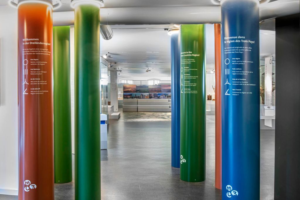 Des colonnes colorées avec des messages de bienvenue multilingues se dressent dans la salle d'exposition.