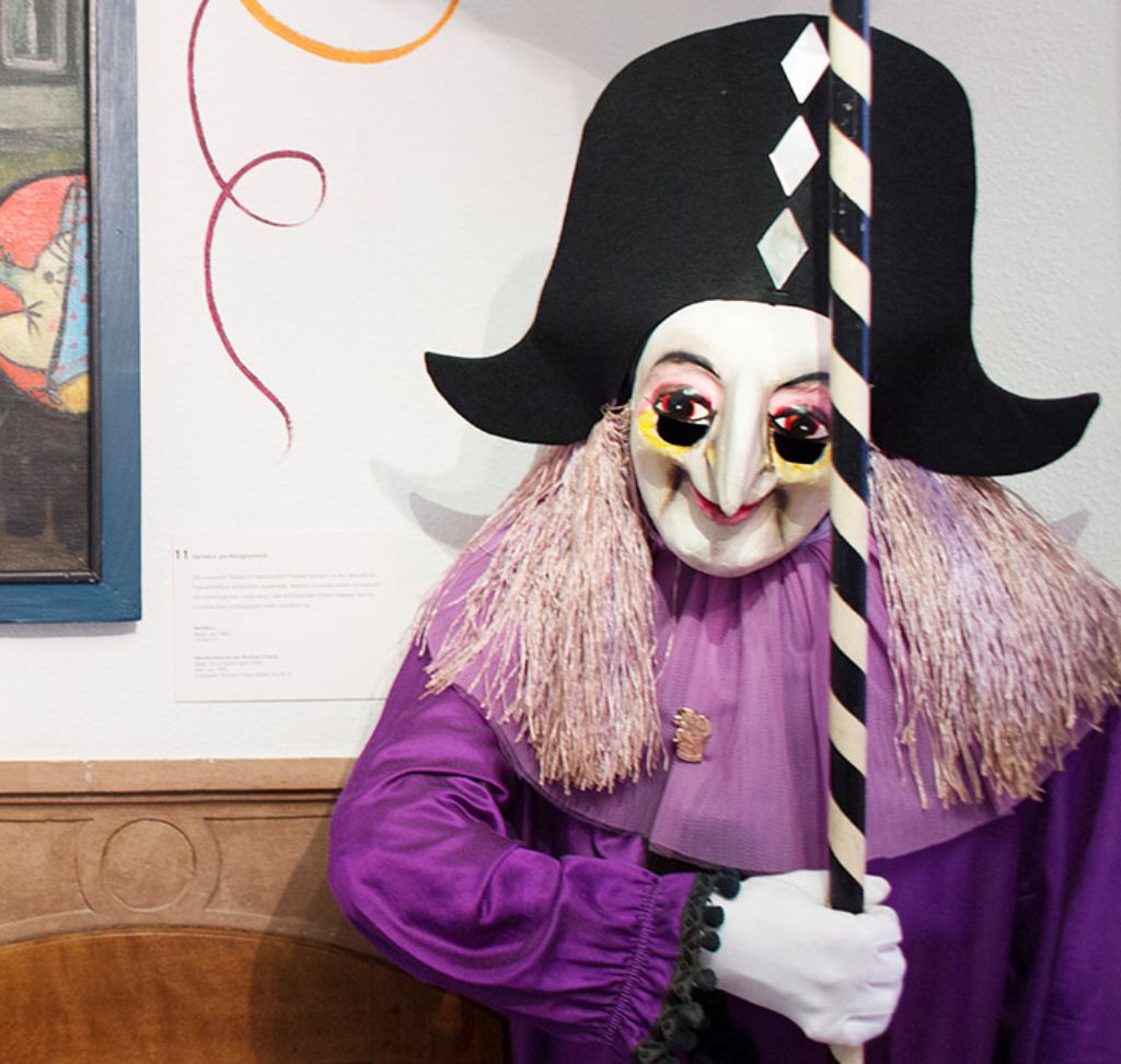 Un arlequin vêtu de violet est assis sur un banc - un personnage de carnaval Il tient une lanterne de poche dans ses mains