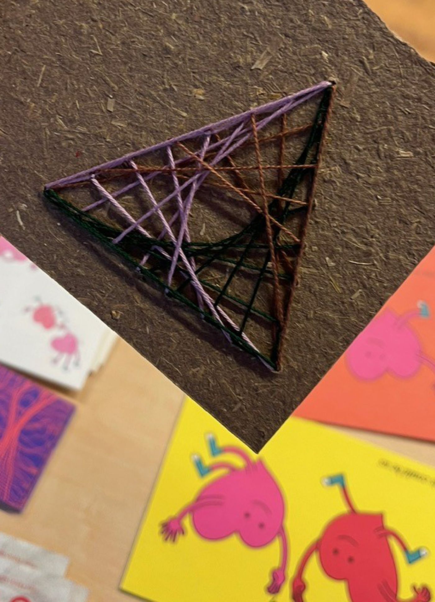 Das Bild zeigt eine bestickte Karte über einer farbigen Zeichnung