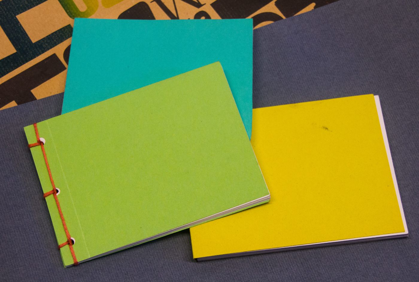 Drei farbige Notizhefte liegen aufeinander, mit Grün, Blau und Gelb als Deckblatt.