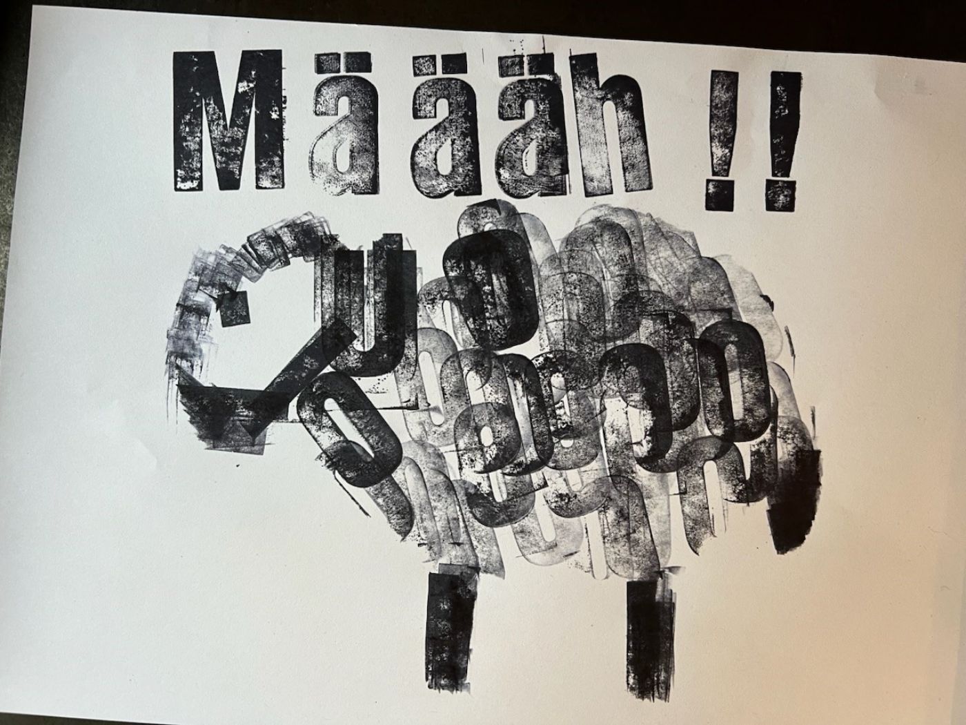Auf einem weissen Papier ist ein schwarzes Schaf aus gestempelten Buchstaben mit "Määh !!" darüber