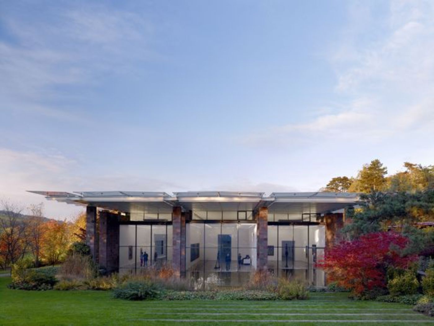 Un bâtiment moderne avec une façade vitrée, entouré d'arbres luxuriants et d'une pelouse verte.