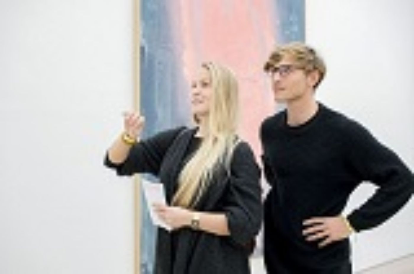A woman and a man stand before a large painting, engaging in an animated discussion.