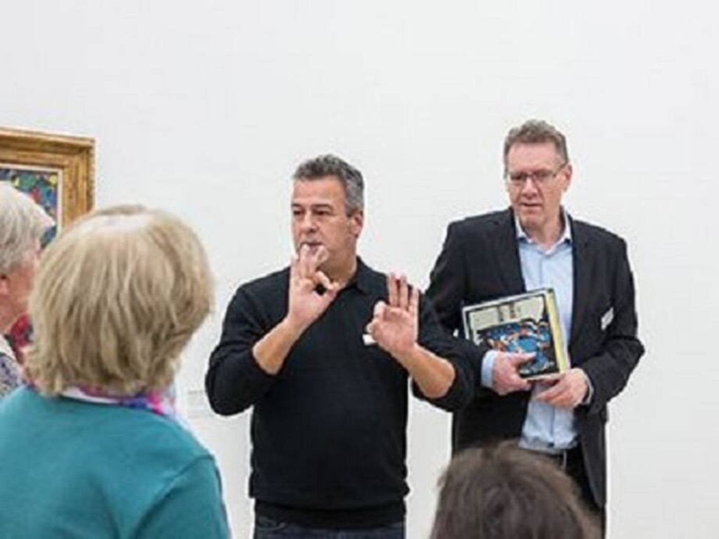 A sign language interpreter explains to a group of people in a bright exhibition space