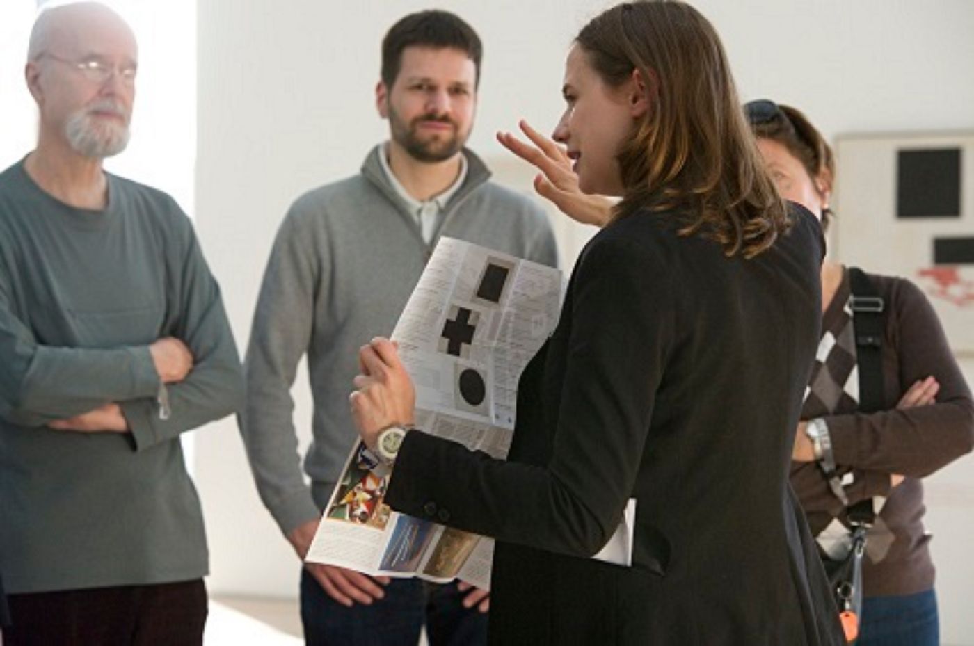 A woman explains an artwork to a small group while holding brochures