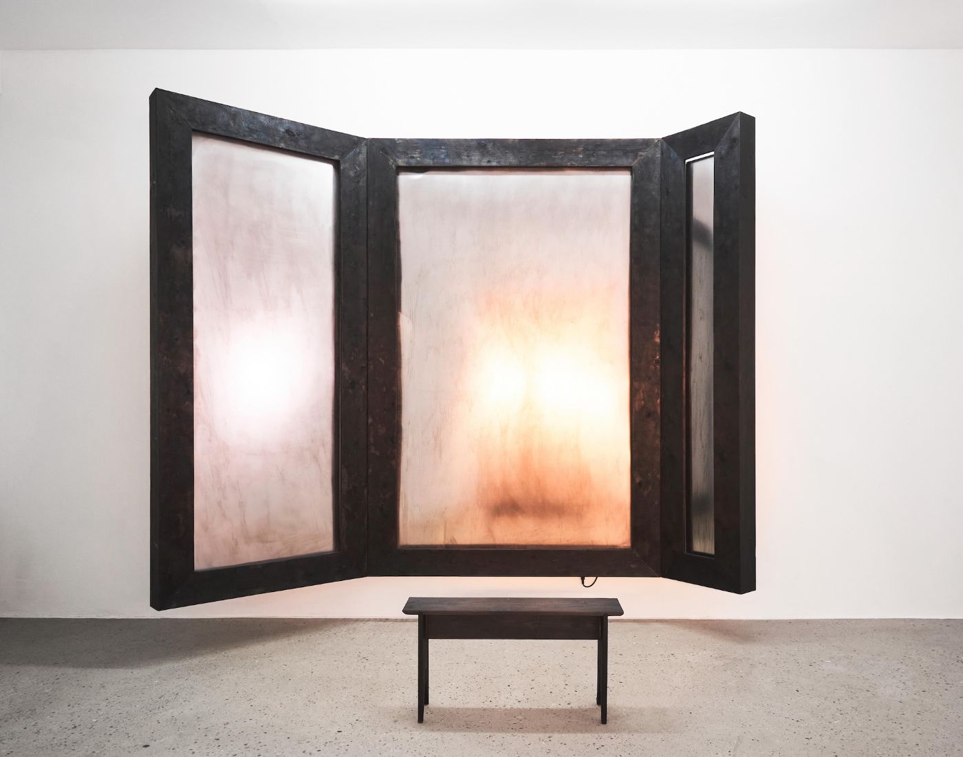 Ein grosser, dreiteiliger, dunkler Rahmen mit leuchtenden, durchscheinenden Flächen dahinter
