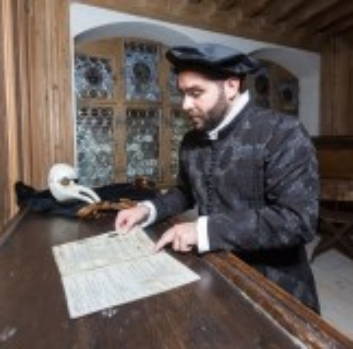 Ein Mann in historischer Kleidung studiert alte Manuskripte an einem Holztisch