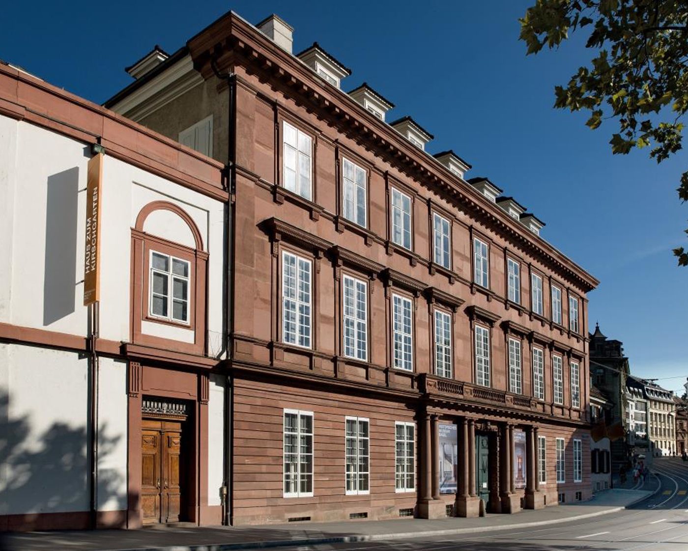 Auf dem Bild ist ein grosses Gebäude im klassizistischen Stil mit roten Fassaden zu sehen