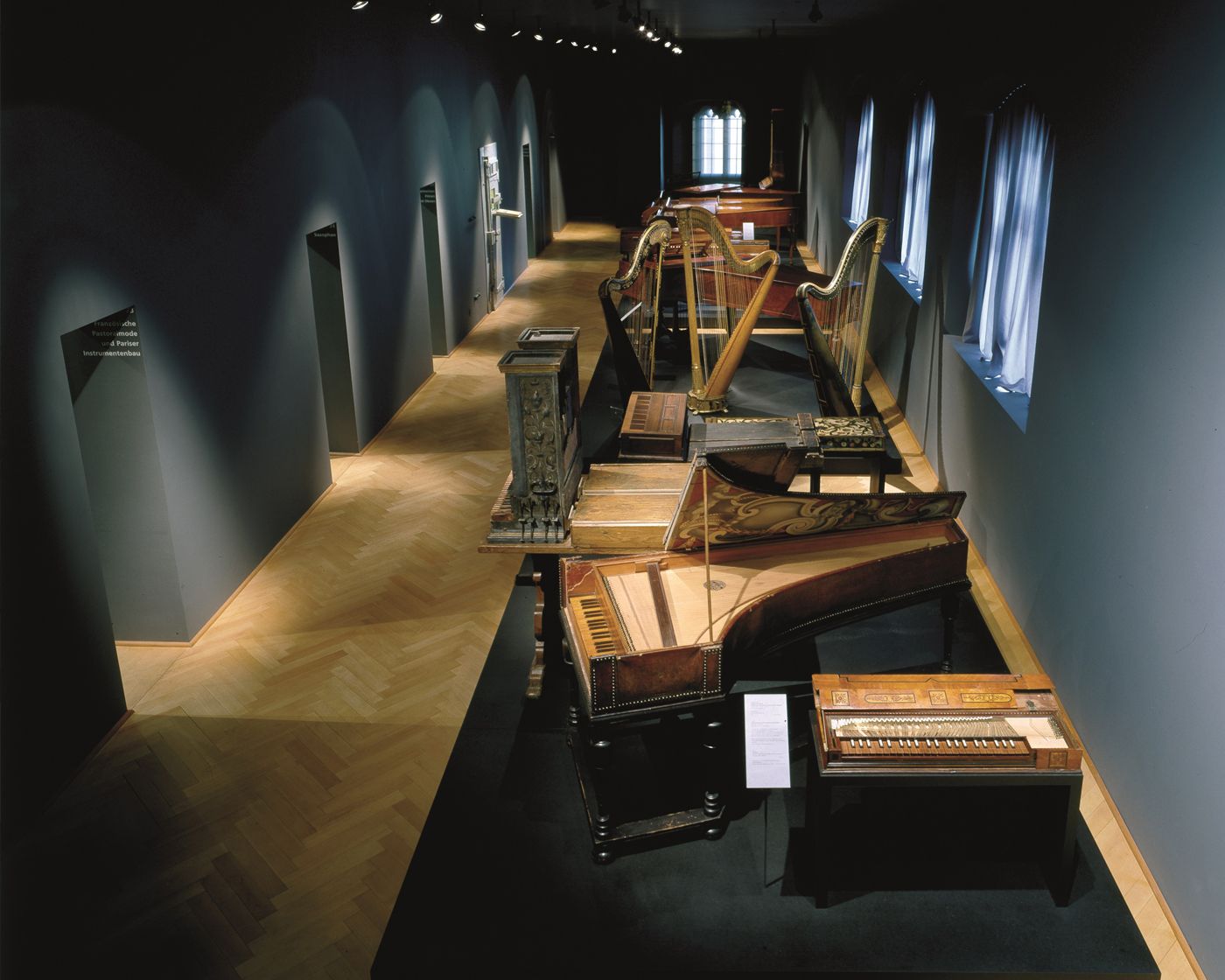 Eine Reihe historischer Tasteninstrumente und Harfen steht aufwendig inszeniert im Ausstellungsraum