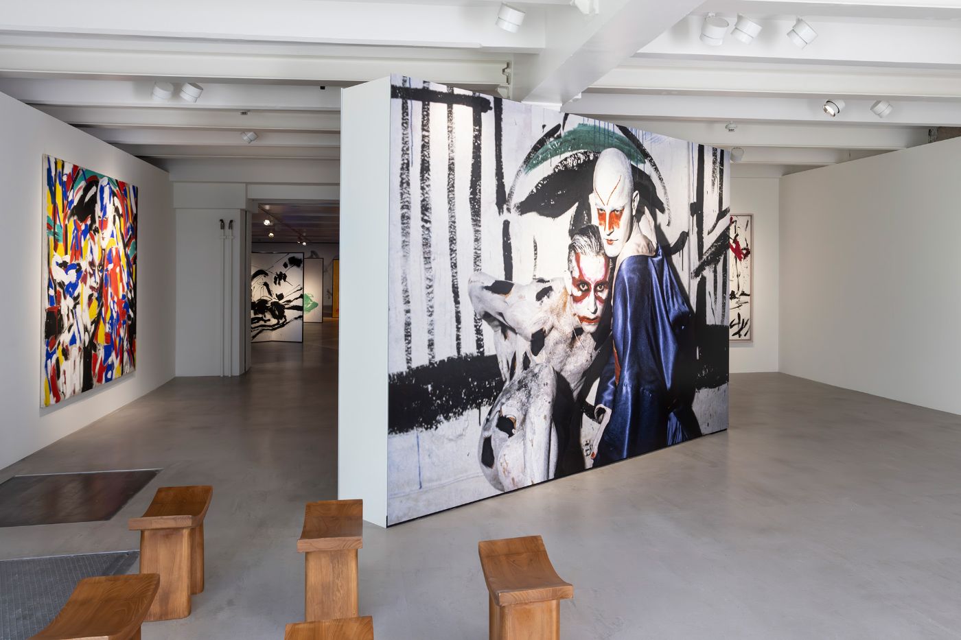 Eine Galerie zeigt bunte und monochrome Kunstwerke mit minimalistischen Holzbänken im Vordergrund