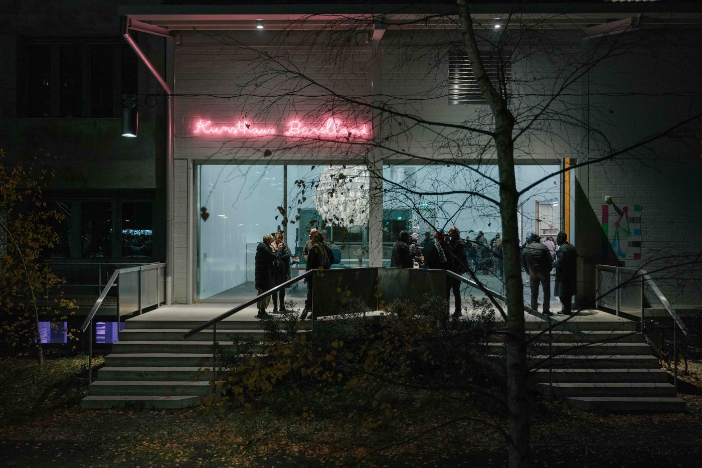 Am Abend verweilen Menschen vor einem modern beleuchteten Gebäude und unterhalten sich