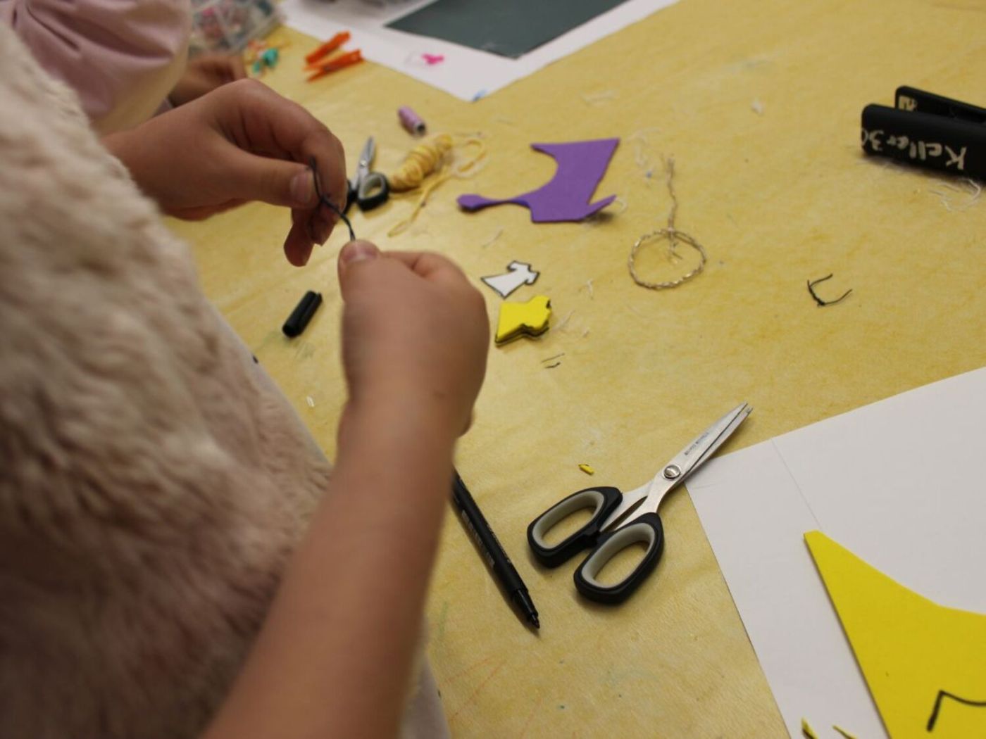 Auf einem Tisch schneiden Hände farbiges Papier, Schere und Stifte liegen bereit