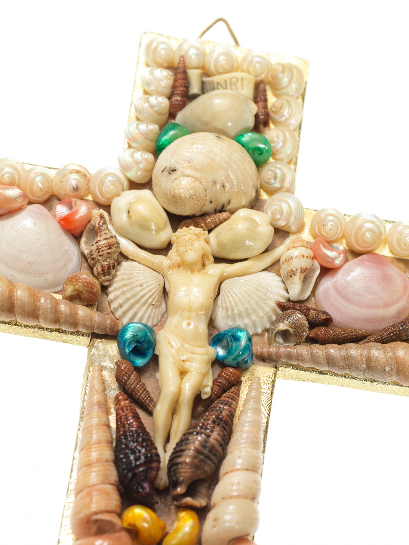 Kreuz, das mit beigen und rosa Muscheln verziert ist und in dessen Mitte ein Jesusfigürchen aufgeklebt ist.