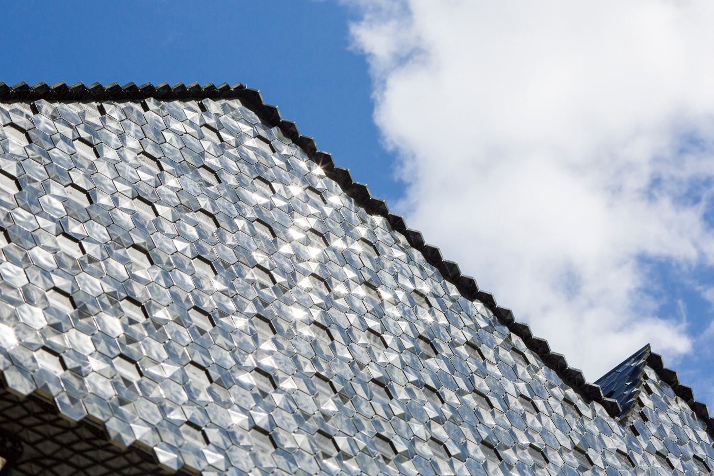 Roof section with hexagonal tiles shimmering in the sunlight, blue sky and white clouds above.