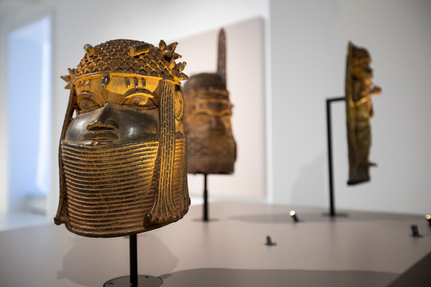 Auf einem Podest in einem Ausstellungssaal steht ein Bronzekopf. Auffällig sind die Kopfbedeckung und der Halsschmuck.
