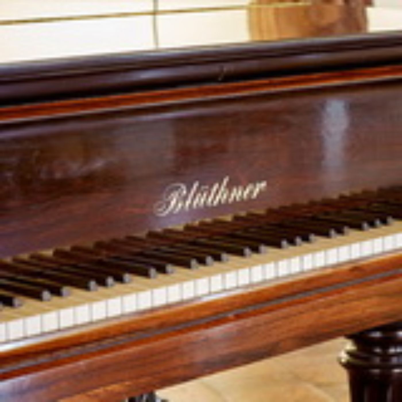 Ein alter Blüthner-Flügel mit warmem Holzton verweilt in einem gemütlichen Raum