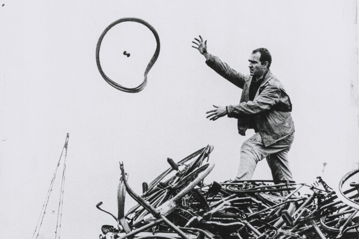 A man throws a bicycle tire into the air over a large pile of old bicycle parts