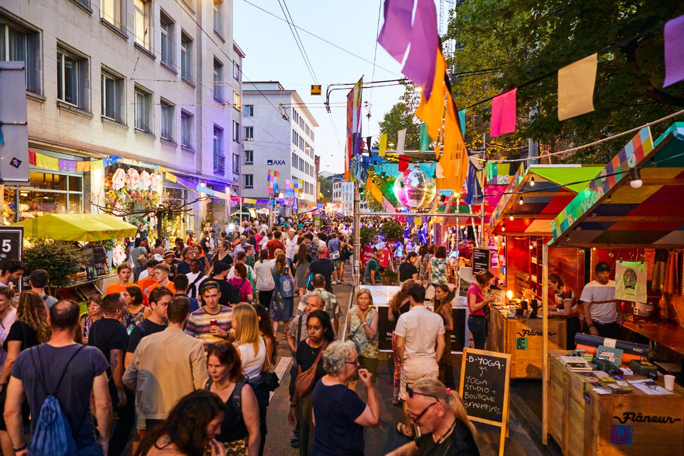 Viele Menschen schlendern durch eine bunte, belebte Strassenfestszene mit Dekorationen