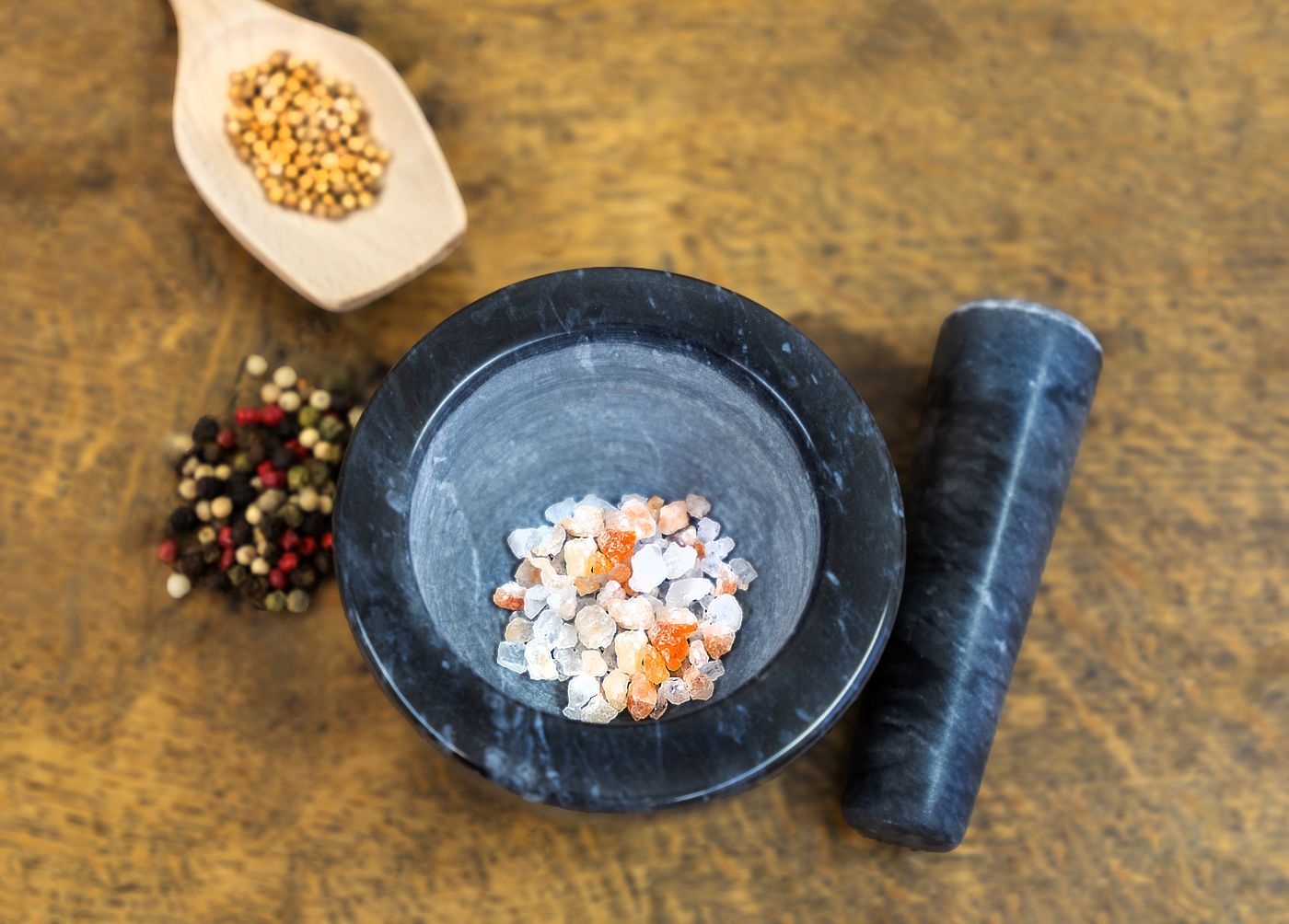 Steinmörser mit Salz, daneben andere Gewürze wie Pfeffer in verschiedenen Farben