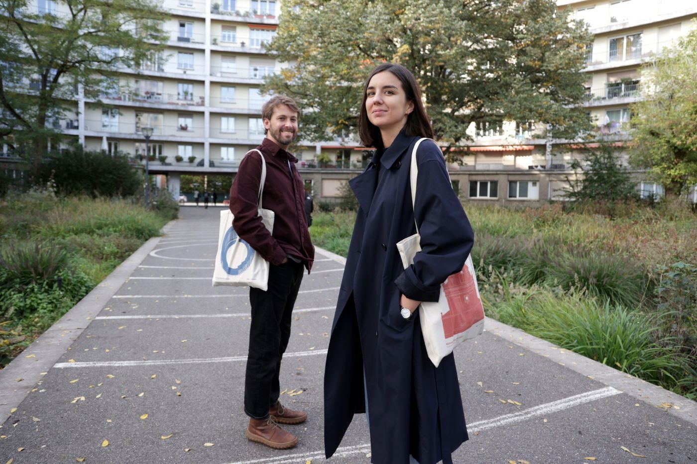 Zwei Personen stehen auf einem Gehweg, umgeben von hohen Gebäuden und Natur