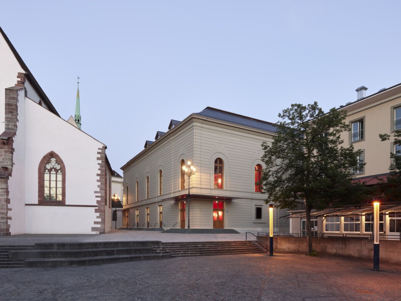 Ein historisches Gebäude bei Abenddämmerung mit beleuchteten Fenstern und einem Baum im Vordergrund.