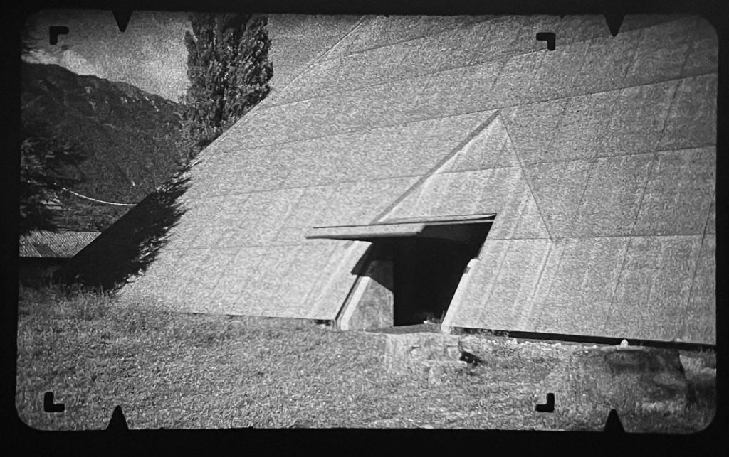 Eine Aussenaufnahme zeigt eine massive, pyramidenartige Struktur mit dreieckigem Eingang.