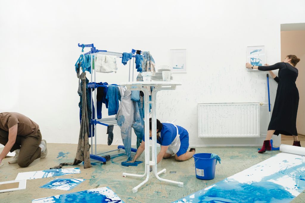 Drei Personen arbeiten in einem Raum mit blauen Flecken an Wänden und Boden