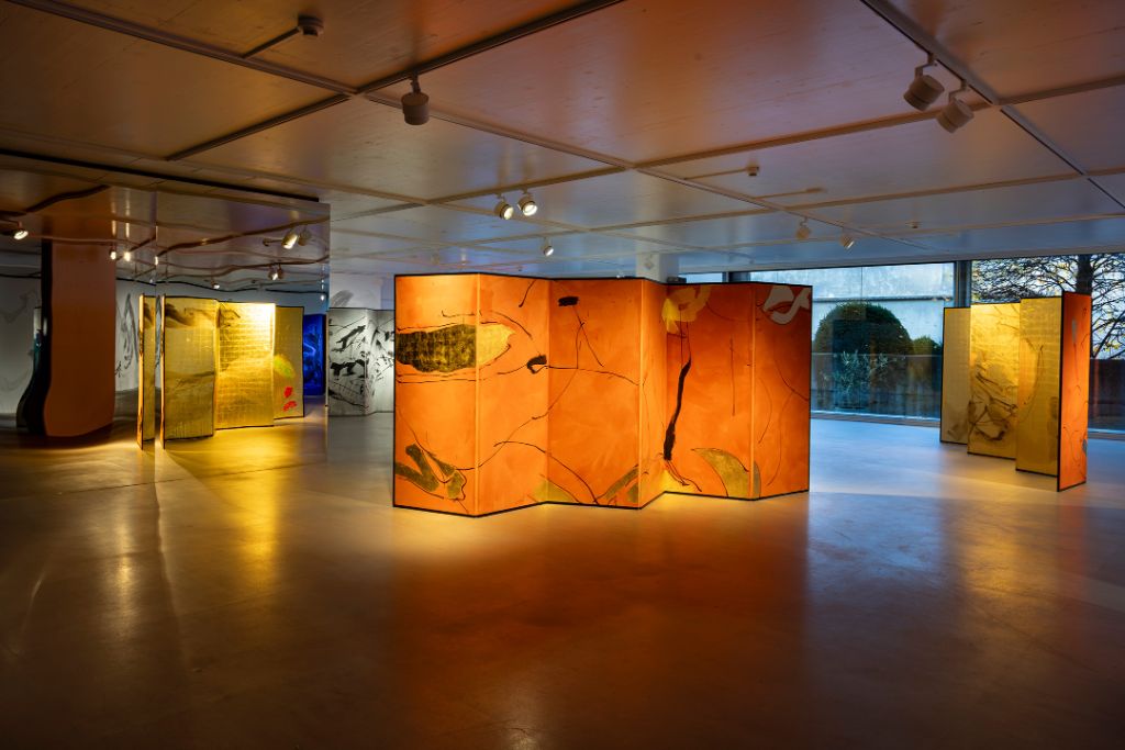 In einem modernen Raum stehen kunstvolle Paravents mit warmen Farben und abstrakten Mustern beleuchtet.