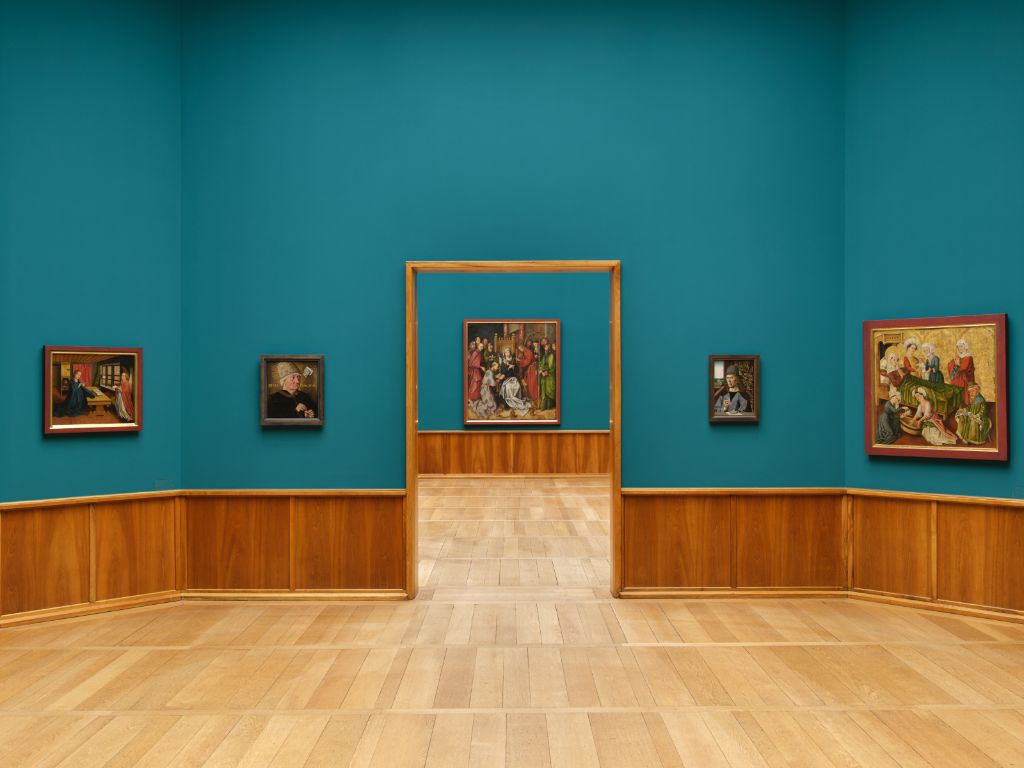 Ein heller Ausstellungsraum zeigt Gemälde und eine Skulptur auf glänzenden Holzböden