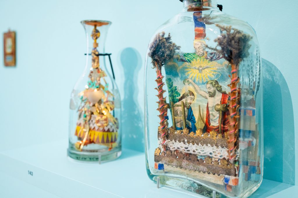 Glasflaschen, in denen aus Papier ganze Szenen gestaltet wurden, rund um Heiligenfiguren