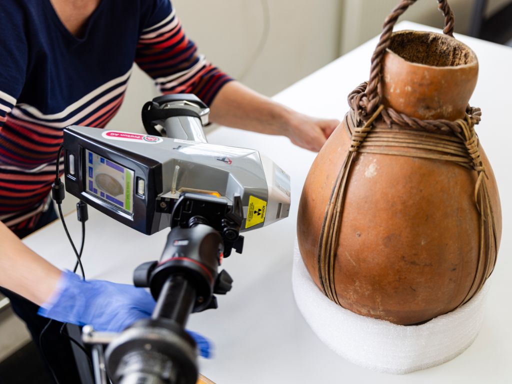 A brown jug stands on a table. A camera is filming it.