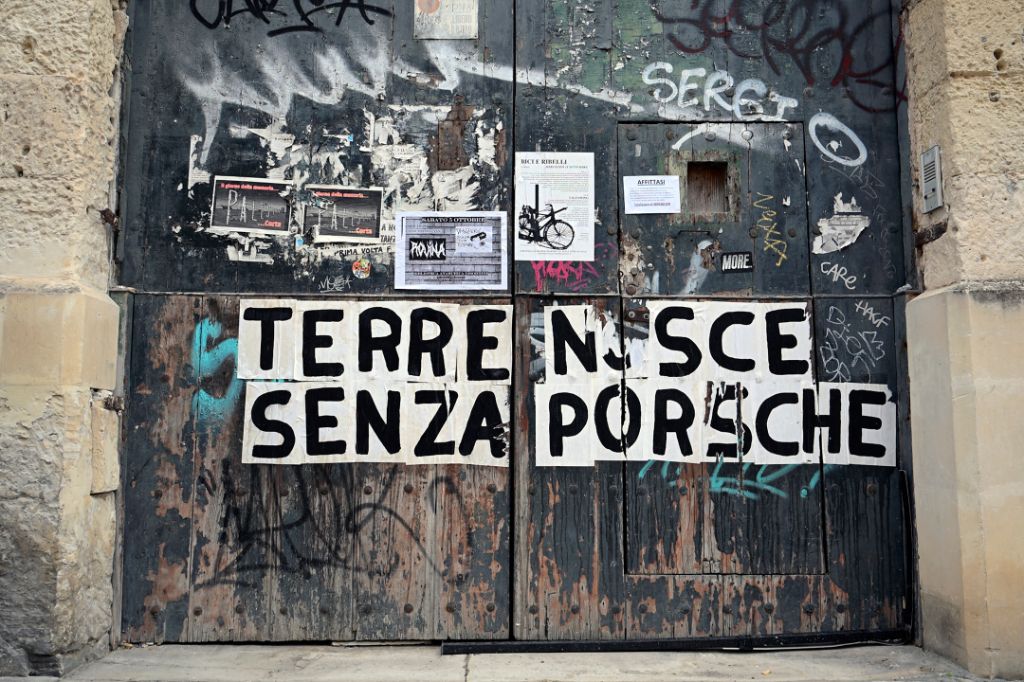 An old door covered in graffiti shows posters and the phrase “Terre Nsce Senza Porsche.”