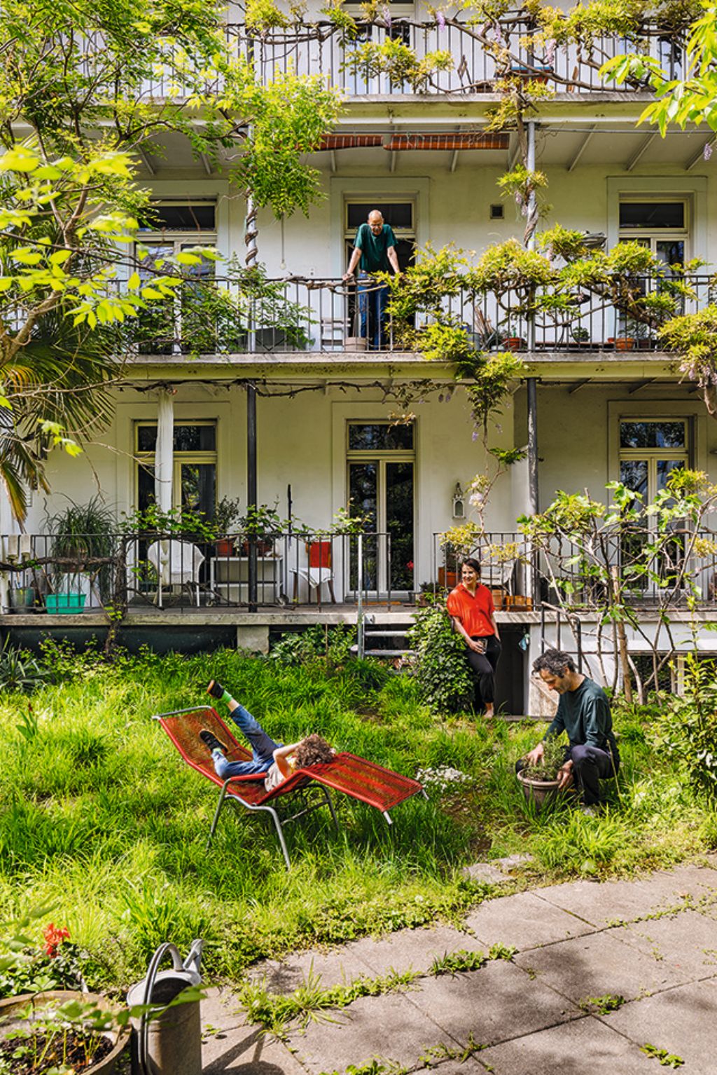 Im grünen Innenhof eines Wohngebäudes relaxen Menschen, während Pflanzen die Balkone säumen